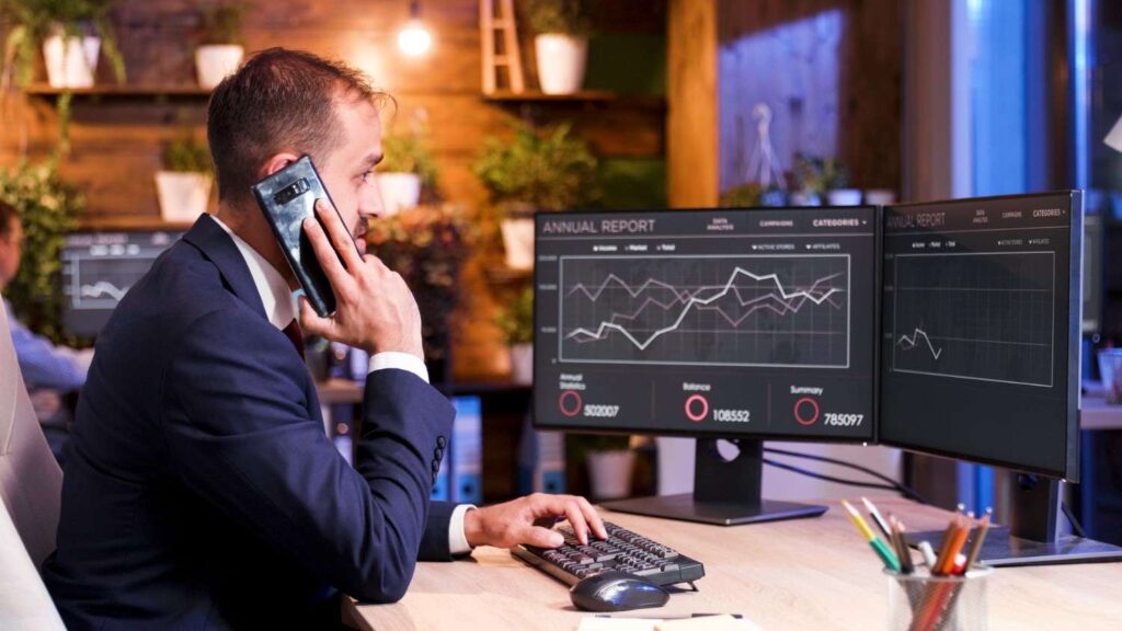 manager speaks phone while analyzing some graphics monitor two screens (1)